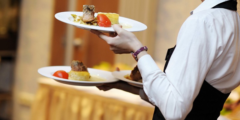 Waitress carrying three plates with meat dish